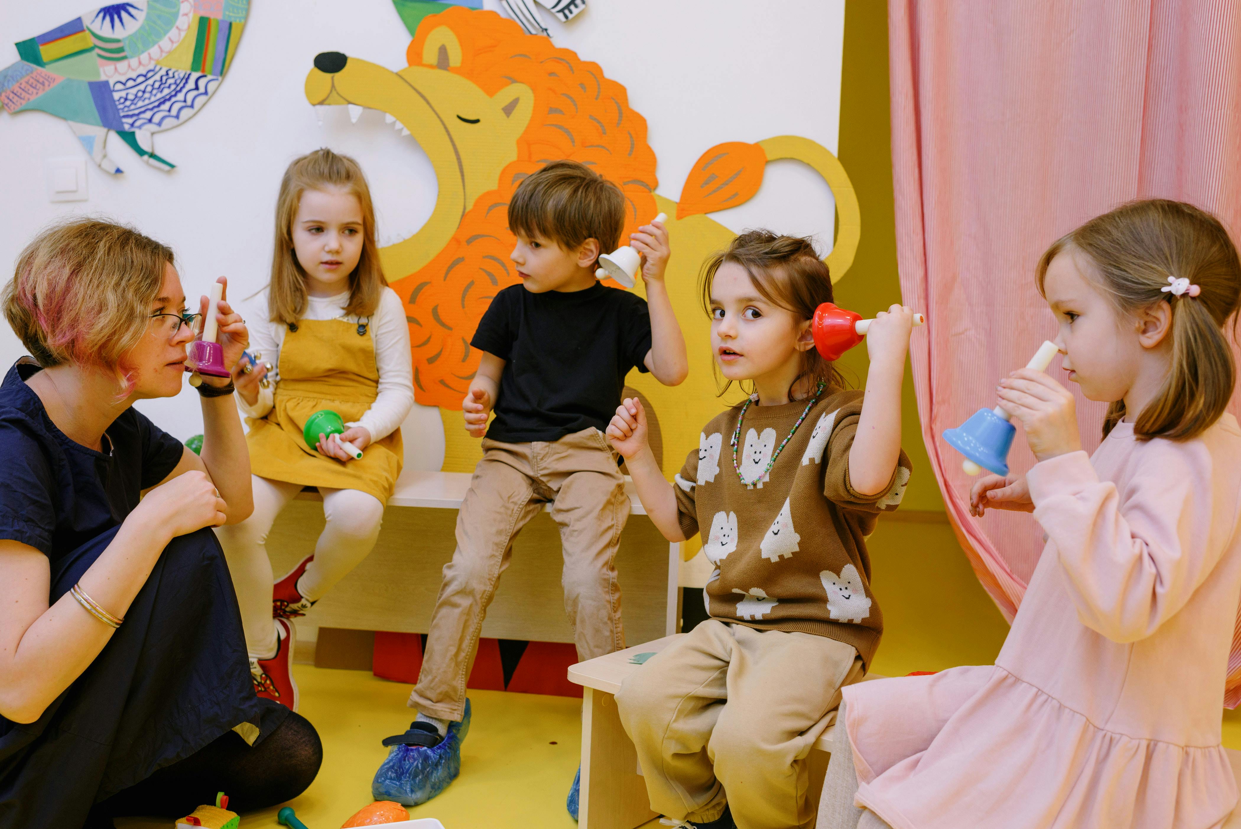 Een kinderleidster geeft vier kinderen muziekles met een bel